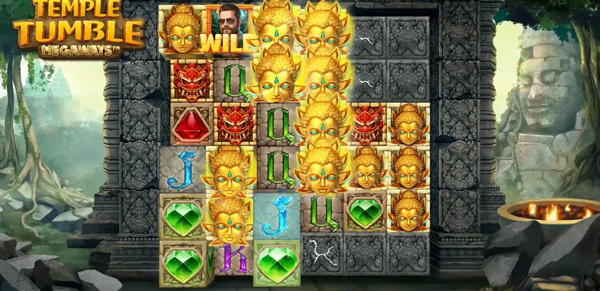 “A Temple Tumble Megaways slot game screen shows stacked golden deity masks forming a large win cluster inside an ancient stone temple with jungle ruins and glowing torches in the background.”